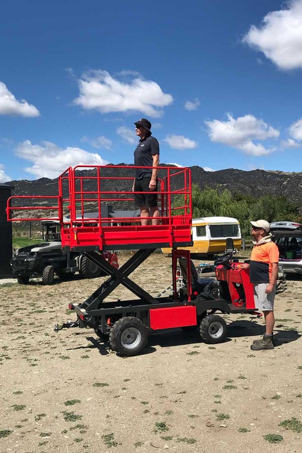 red pickman PICCA electric work platform in raised mode with person standing on the work platform. New Zealand hills in background